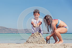 Cute little boy and a girl building a sand castle on a tropical sea shore