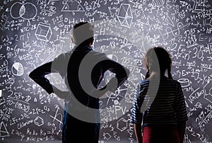 Cute little boy and girl in front of a big blackboard.