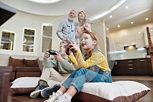 Cute little boy and girl having fun at home, playing video games while sitting on the floor, spending time with