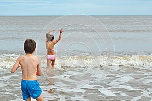 Cute little boy and girl, playing in wave on beach