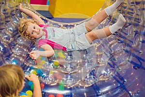Cute little boy and girl playing in Zorb a rolling plastic cylinder ring with a hole in the middle, intdoor