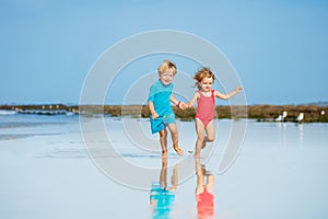 Cute little boy and girl run on sand beach over ocean hold hands