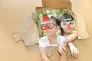 Cute little boy and girl wearing funny Christmas glasses making funny faces in torn paper wall