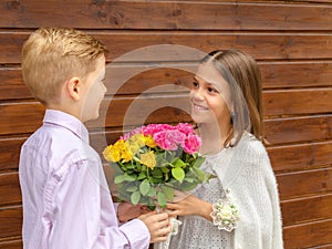 Cute little boy giving bouquet of flowers to charming little lady Ã¢â¬â smiling girl in love receiving yellow and pink roses