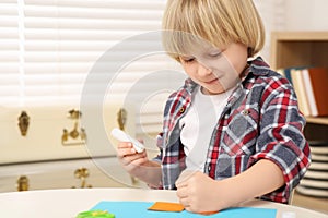 Cute little boy with glue stick at desk in room. Home workplace