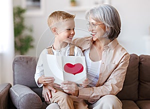 Cute little boy grandson congratulating smiling grandmother and giving handmade greeting card