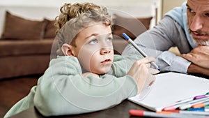 Cute little boy grandson drawing with colored felt tip pens with his grandfather while sitting at table at home