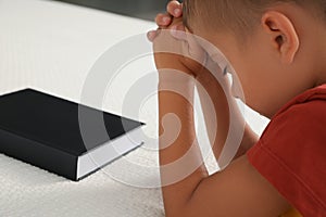 Cute little boy with hands clasped together saying bedtime prayer over Bible at home, closeup