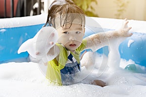 Cute little boy having fun playing with bubbles in an inflatable pool on a summer vacation