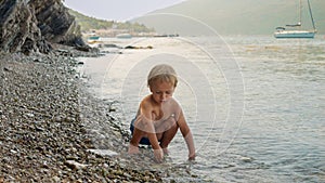 Cute little boy having fun on the sea beach and throwing stones in sea waves