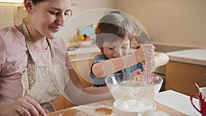 Cute little boy having fun and smiling while helping mother mixing dough in big bowl. Children cooking with parents