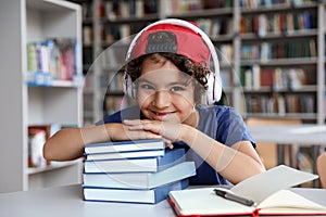 Cute little boy with headphones and books at table in reading room