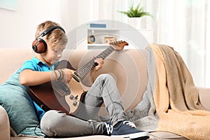 Cute little boy with headphones playing guitar on sofa