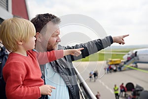 Cute little boy and his father pointing at airplanes on observation deck at airport of small european town before flight. Charming