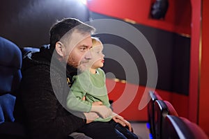 Cute little boy with his father watching cartoon movie in the cinema