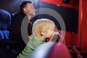 Cute little boy with his father watching cartoon movie in the cinema