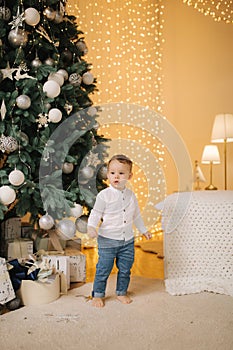 Cute little boy at home by the big Christmas tree looking for presents. Happy kid spend time on Holiday and enjoying