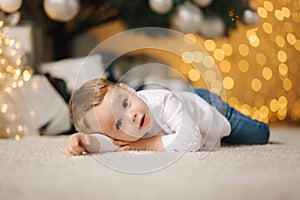 Cute little boy at home by the big Christmas tree looking for presents. Happy kid spend time on Holiday and enjoying