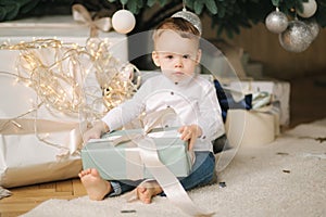 Cute little boy at home by the big Christmas tree looking for presents. Happy kid spend time on Holiday and enjoying