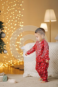 Cute little boy at home by the big Christmas tree looking for presents. Happy kid spend time on Holiday and enjoying