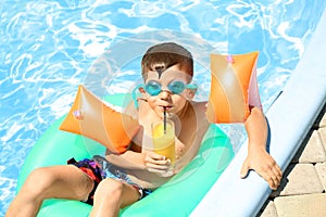 Cute little boy with inflatable ring drinking juice in swimming pool