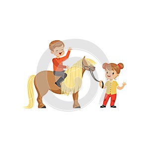 Cute little boy jockey sitting on pony horse, beautiful girl leading horse by the bridle, childrens equestrian sport