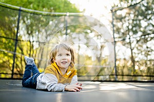 Cute little boy jumping on a trampoline in a backyard on warm and sunny summer day. Sports and exercises for children