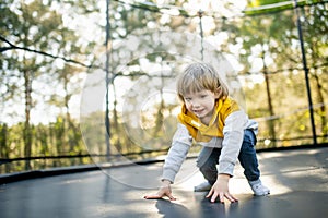 Cute little boy jumping on a trampoline in a backyard on warm and sunny summer day. Sports and exercises for children