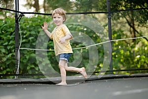 Cute little boy jumping on a trampoline in a backyard on warm and sunny summer day. Sports and exercises for children. Summer