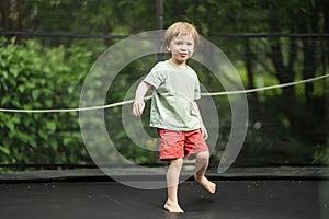 Cute little boy jumping on a trampoline in a backyard on warm and sunny summer day. Sports and exercises for children. Summer