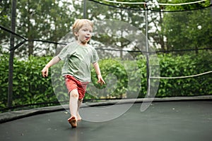 Cute little boy jumping on a trampoline in a backyard on warm and sunny summer day. Sports and exercises for children. Summer