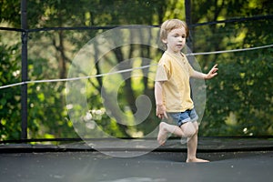 Cute little boy jumping on a trampoline in a backyard on warm and sunny summer day. Sports and exercises for children. Summer