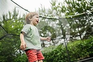 Cute little boy jumping on a trampoline in a backyard on warm and sunny summer day. Sports and exercises for children. Summer