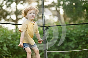 Cute little boy jumping on a trampoline in a backyard on warm and sunny summer day. Sports and exercises for children. Summer