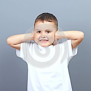 Cute little boy kid covering his ears with hands against gray background