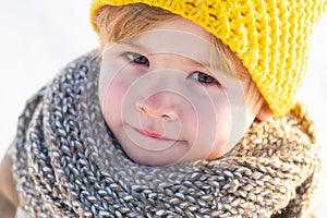 Cute little boy kid in winter clothes walking under snow. Child in blue jacket and yellow hat walks in snow-covered