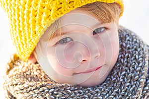 Cute little boy kid in winter clothes walking under snow. Child in blue jacket and yellow hat walks in snow-covered