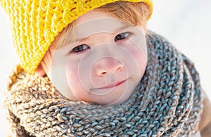 Cute little boy kid in winter clothes walking under snow. Child in blue jacket and yellow hat walks in snow-covered