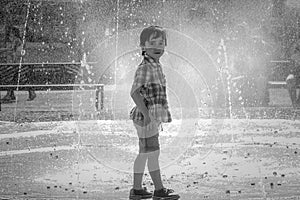 Cute little boy is laughing and having fun running under a water fountain