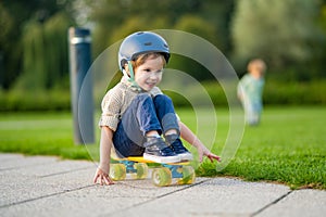 Cute little boy learning to skateboard on beautiful summer day in a park. Child wearing safety helmet enjoying skateboarding ride