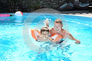 Cute little boy learning to swim with father in pool