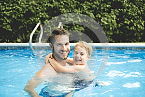 Cute little boy learning to swim with parents in pool
