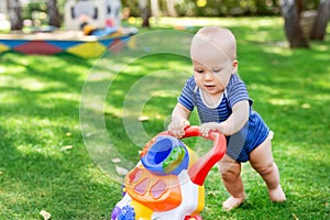 Cute little boy learning to walk with walker toy on green grass lawn at backyard. Baby laughing and having fun making first step a