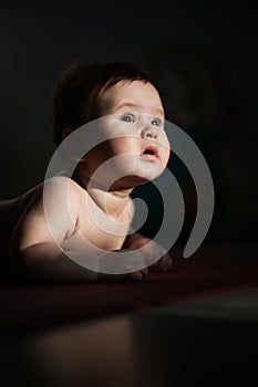 A cute little boy lies on his forearms on the floor. Vertical photo.