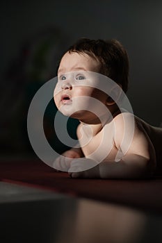 A cute little boy lies on his forearms on the floor. Vertical photo.