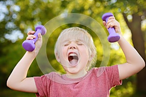 Cute little boy lifting dumbbells outdoors