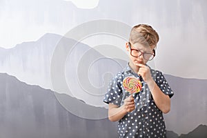 Cute little boy with lollipop near grey wall