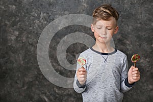 Cute little boy with lollipops on grey background