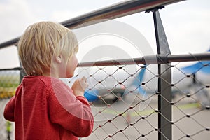 Cute little boy look at airplanes on observation deck at airport of small european town before flight. Charming kid passenger