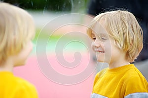 Cute little boy looks in distorting mirror in play center. Child playing on outdoor playground